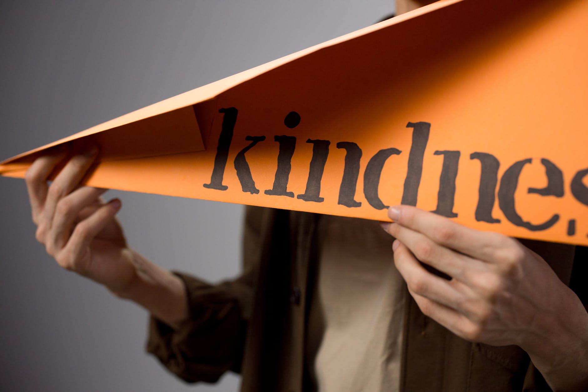 holding a large paper plane with the word kindness written on it